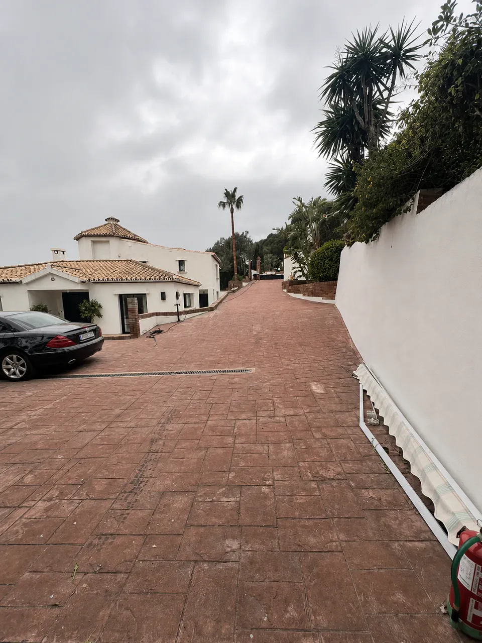 Driveway before: worn red block paving between white walls